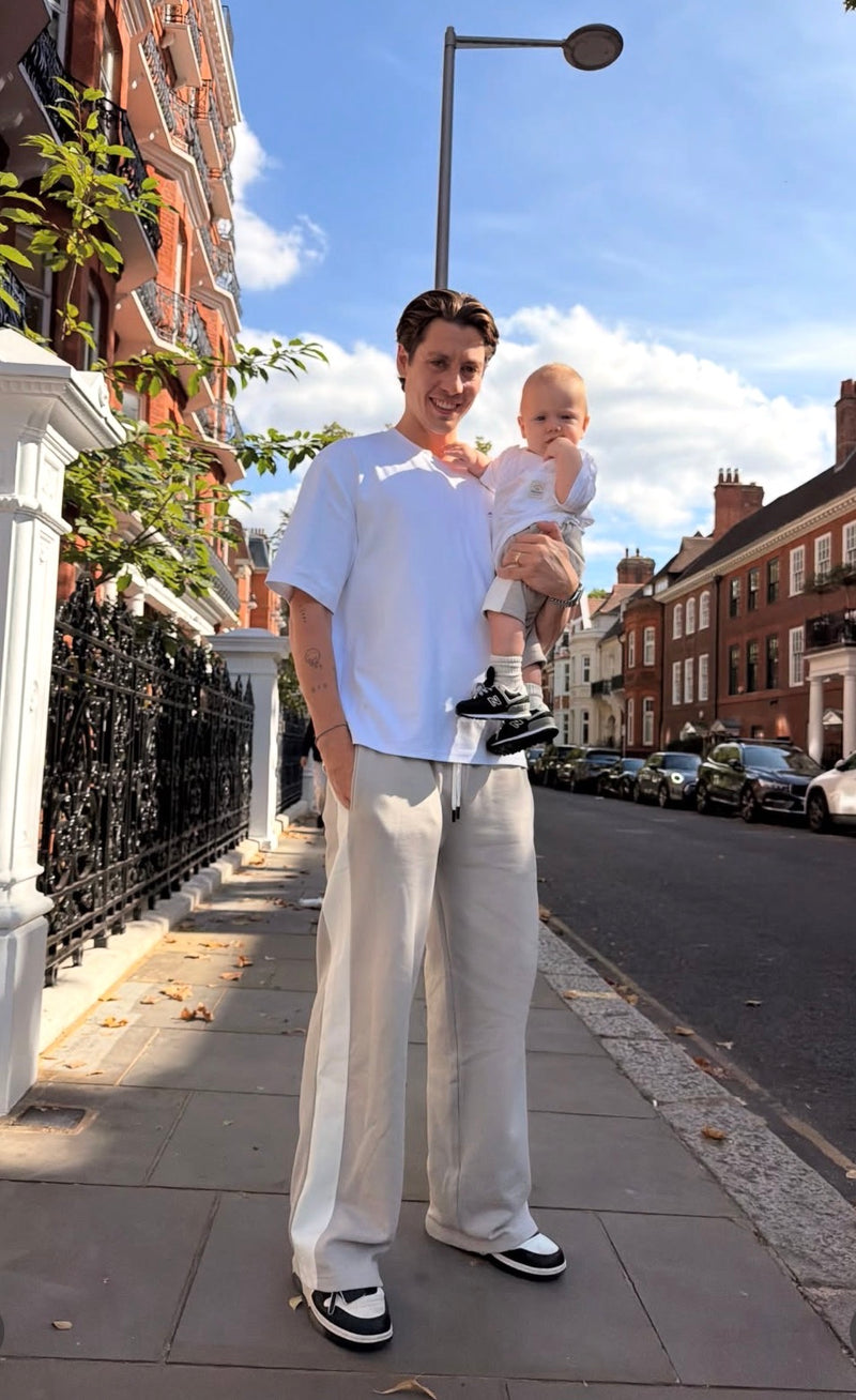 Sam Vanderpump holding his baby while wearing matching white MANCUB T-shirts on a city street