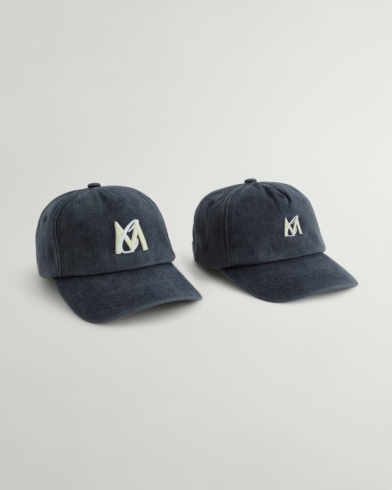 Two navy blue baseball caps with a white embroidered stylized 'M' logo on the front, displayed side-by-side on a light gray background.