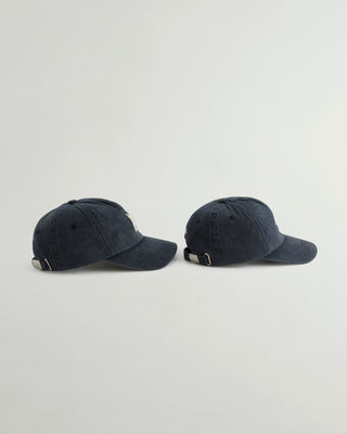 Two dark navy blue washed baseball caps shown from the side against a light gray background.