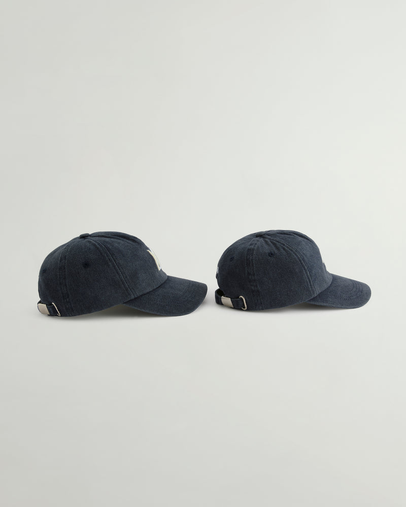 Two dark navy blue washed baseball caps shown from the side against a light gray background.
