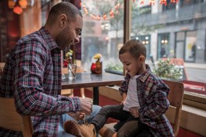 Father teaching son to tie shoe lace wearing matching MANCUB checked shirts