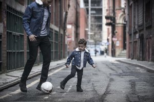 Father and son in denim jackets playing football in the street
